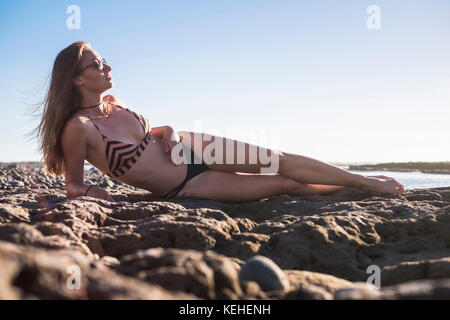 Donna caucasica che si posa sulla spiaggia indossando bikini Foto Stock