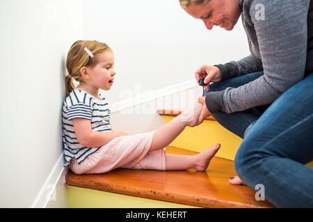 Madre caucasica pittura toenails di figlia su scala Foto Stock