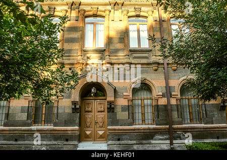 Vecchio edificio multicolore di tufo con archi scolpiti,colonne e cornicioni circondato da alberi Foto Stock