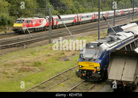 Virgin Trains servizi della East Coast passando per la locomotiva diesel Direct Rail Services classe 68 68030 in attesa nei binari Holgate a sud della stazione di York, Regno Unito. Foto Stock