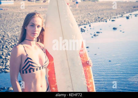 La donna caucasica permanente sulla spiaggia surfboard holding Foto Stock