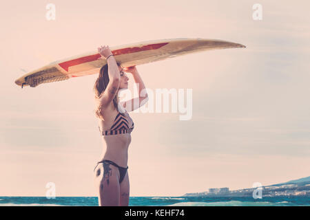 La donna caucasica permanente sulla spiaggia surfboard holding Foto Stock