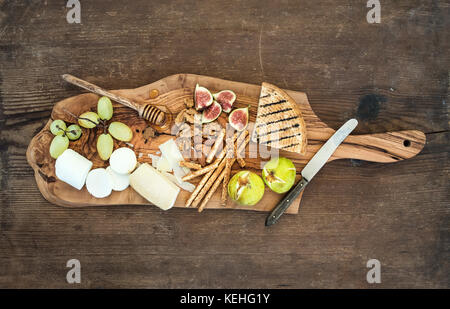 Vino antipasti set: selezione di formaggi, miele, uva, mandorle, noci, grissini, figure in legno d'ulivo che serve al di sopra della scheda sfondo rustico , parte superiore vi Foto Stock