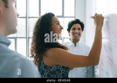 Imprenditrice scrivere sulla lavagna in riunione Foto Stock