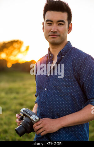 Sorridente uomo cinese che tiene la macchina fotografica nel campo Foto Stock