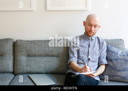 Uomo caucasico seduto su divano scrivere in blocco note Foto Stock