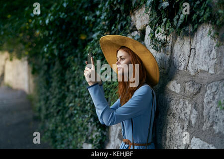 Donna caucasica fotografando con il telefono cellulare vicino muro di pietra Foto Stock