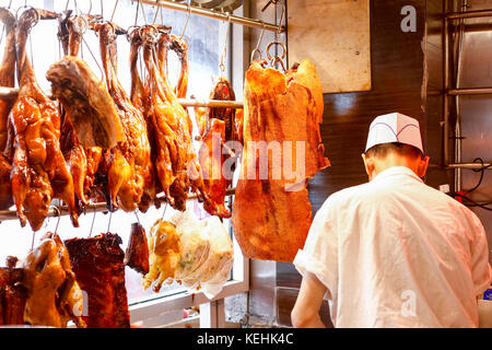 Macellaio in piedi vicino alla carne appesa Foto Stock