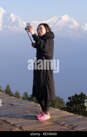 Turistica prendendo un selfie sul suo telefono cellulare con la catena Hannapurna come sfondo. Poon Hill, Nepal. Foto Stock