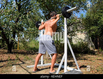 L'uomo assume un bar per eseguire squat. esercizi di bodybuilding. sport nel cortile posteriore Foto Stock