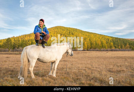 Il mongolo uomo seduto su un cavallo e fumare una sigaretta Foto Stock