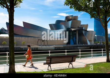 La donna passa accanto al Museo Guggenheim dell'architetto Frank Gehry attraverso il fiume Nervion a Bilbao, Paesi Baschi, Spagna Foto Stock