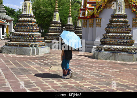 Giovane donna prende ombra sotto un ombrellone come lei passeggiate attraverso il Wat Pho tempio a Bangkok, in Thailandia Foto Stock