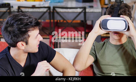 Due giovani uomini in posa sul divano e sperimentare gli occhiali VR mentre il trascorrere del tempo insieme. Foto Stock
