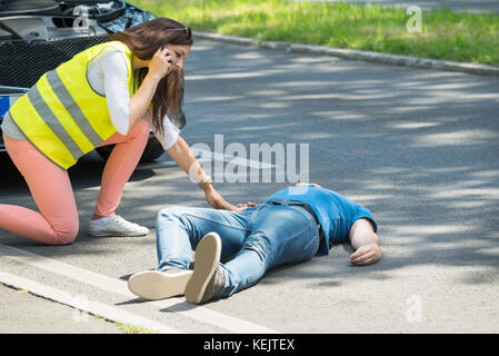 Donna che chiama per aiuti di emergenza guardando uomo ferito dopo un incidente Foto Stock