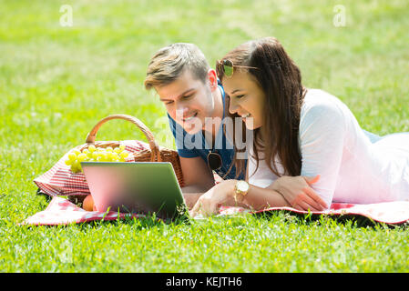 Felice coppia utilizzando laptop mentre giaceva in posizione di parcheggio Foto Stock