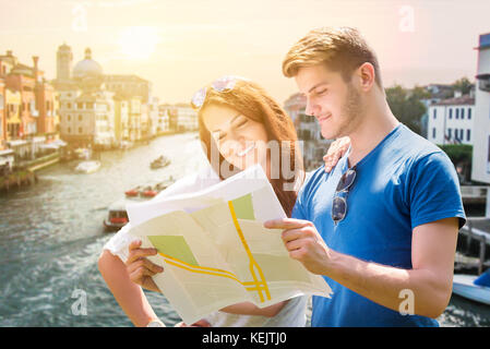 Coppia sorridente alla ricerca per la loro destinazione con la mappa di venezia, Italia Foto Stock