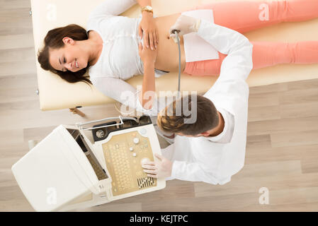 Vista in elevazione di un medico di sesso maschile utilizzando Sonogram sul paziente femmina nella sala esame Foto Stock