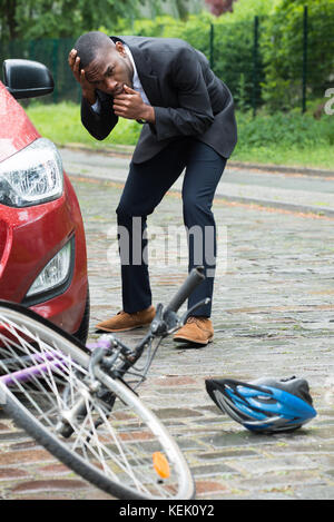 Scioccato driver maschio con le mani sulla testa guardando bicicletta dopo una collisione su strada Foto Stock