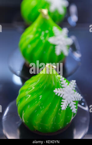 Moderno mousse francese torta decorata in stile natalizio coperto con smalto verde specchio e il cioccolato bianco il simbolo del fiocco di neve. Foto Stock