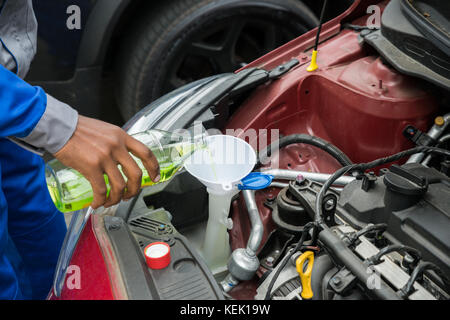 Close-up di meccanico versando olio nel motore per auto Foto Stock