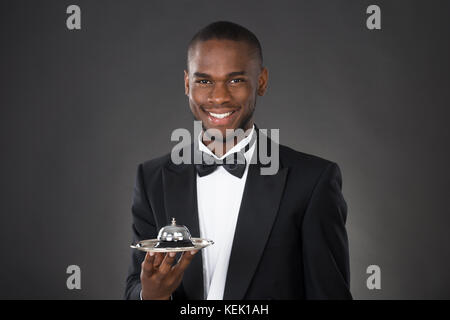 Ritratto di Felice cameriere africano Holding campana di servizio Foto Stock