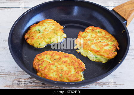 Frittelle di zucchini su un nero padella su uno sfondo di legno. Il mangiare sano concetto. passo per passo per la cottura Foto Stock