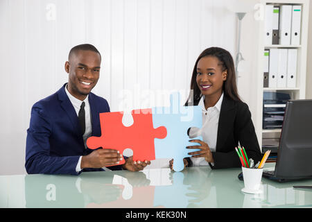 Giovani imprenditori felice azienda puzzle al desk e mostrando la loro unità Foto Stock