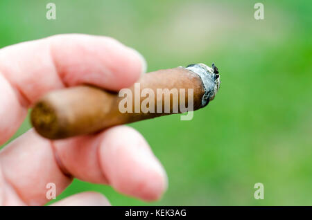 Close-up foto di una mano con le dita in possesso di un sigaro di masterizzazione con in primo piano sfocato Foto Stock