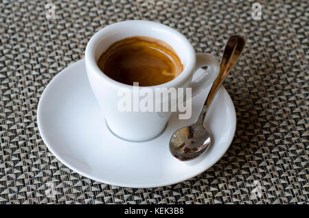 Primo piano del caffè espresso in porcellana bianca cup sul piattino con cucchiaio in piedi sul tavolo Foto Stock