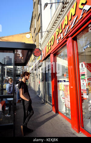 Giovane uomo in piedi alla fermata bus guardando nel ristorante Pizza a Londra in Inghilterra Foto Stock