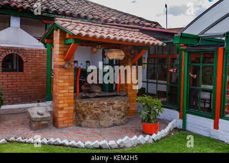 Colombia, Sud America - una sezione del Restaurante El Colonial a Nemocon, nel dipartimento di Cundinamarca con un Vecchio pozzo. Luce del sole del pomeriggio. Foto Stock