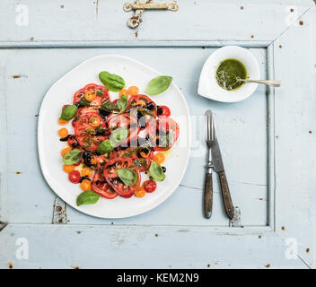 Villaggio mature cimelio di insalata di pomodoro con olio d'oliva e basilico sulla luce blu sullo sfondo di legno, vista dall'alto Foto Stock