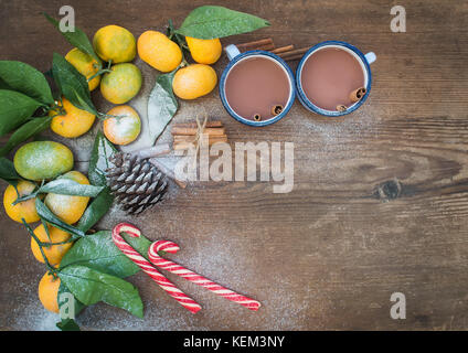 Natale o Capodanno telaio. i mandarini freschi con foglie, bastoncini di cannella, Pigna, cioccolato caldo in tazze e candy canes su legno rustico backgro Foto Stock