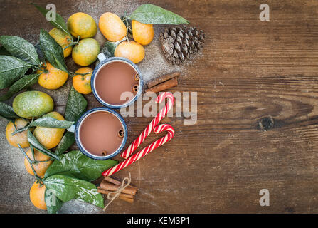 Natale o Capodanno telaio. i mandarini freschi con foglie, bastoncini di cannella, Pigna, cioccolato caldo in tazze e candy canes su legno rustico backgro Foto Stock