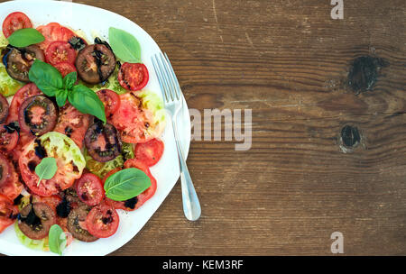 Villaggio mature cimelio di insalata di pomodoro con olio d'oliva e basilico su legno rustico sfondo, vista dall'alto, spazio di copia Foto Stock