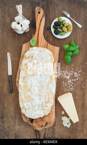 Appena sfornato pane ciabatta con aglio, mediterraneo olive, basilico e parmigiano a servire la scheda sopra rustico sfondo di legno Foto Stock