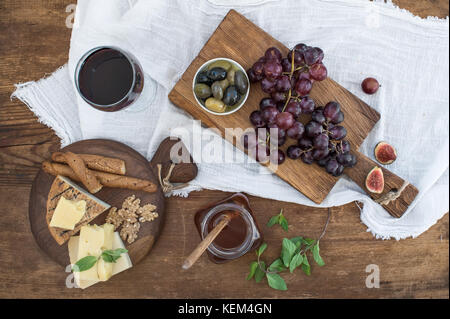 Bicchiere di vino rosso, formaggi, uva, noci, olive, miele e grissini sulla tavola in legno rustico Foto Stock