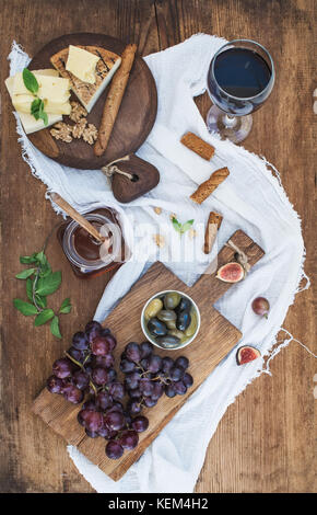 Bicchiere di vino rosso, formaggi, uva, noci, olive, miele e grissini sulla tavola in legno rustico Foto Stock