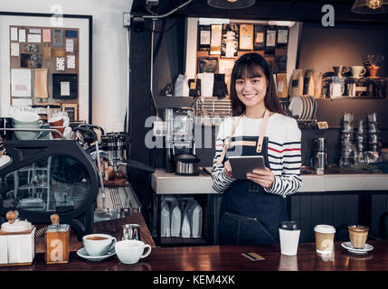 Donna barista prende fine con la compressa,asia cameriera femmina utilizzando dispositivo digitale in coffee shop business al bancone bar in cafe,cibo moderno proprietario busines Foto Stock