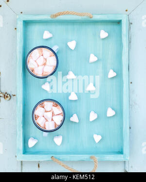 San Valentino annuncio vacanze set. cioccolata calda a forma di cuore marshmallows in smalto vecchio tazze sul turchese che serve il vassoio su blu sullo sfondo di legno Foto Stock