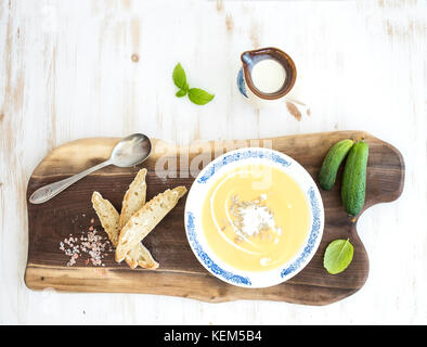 Zuppa di zucca con Crema di basilico fresco, cetrioli e pane in vintage piastra in ceramica su tavola di legno su sfondo bianco, vista dall'alto Foto Stock