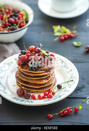 Set colazione. frittelle di farina di grano saraceno con frutti di bosco freschi e miele sulla piastra rustica su tavoli in legno nero. Foto Stock