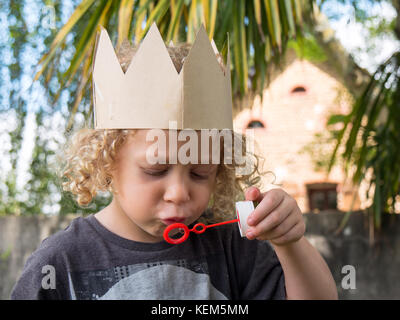 Un piccolo ragazzo biondo facendo bolle di sapone Foto Stock