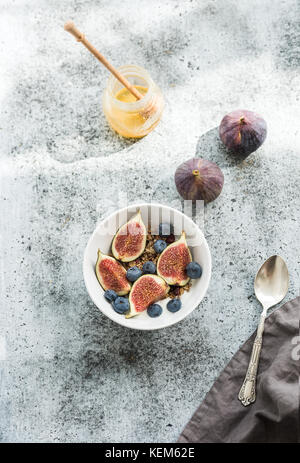 Una sana prima colazione. ciotola di oat granola con yogurt, mirtilli freschi e figure su grunge sfondo grigio Foto Stock