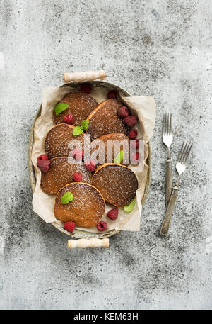 Set colazione. in casa frittelle di farina di grano saraceno con lamponi freschi nel vassoio, cucina igienico, vintage argenteria su grigio Sfondo grunge. Foto Stock