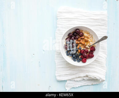 Sana colazione set. ciotola di porridge di avena con frutti di bosco freschi, mandorla e miele oltre il tovagliolo bianco. top view, azzurro sfondo. Foto Stock