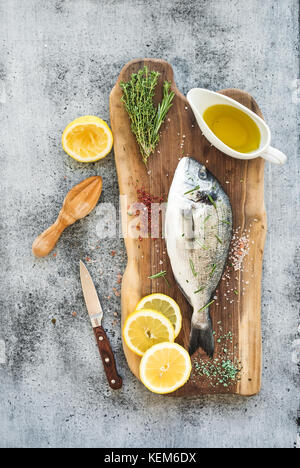 Non cotte fresche dorado o Orate di mare Pesce con limone, erbe, olio e spezie rustico di legno su sfondo grunge Foto Stock