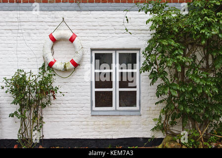 Dipinto di bianco parete in mattoni con finestra, cespugli verdi e alterò il bianco e il rosso salvagente Foto Stock