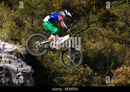 Downhill mountain biker con pantaloncini verde saltando da una caduta Foto Stock